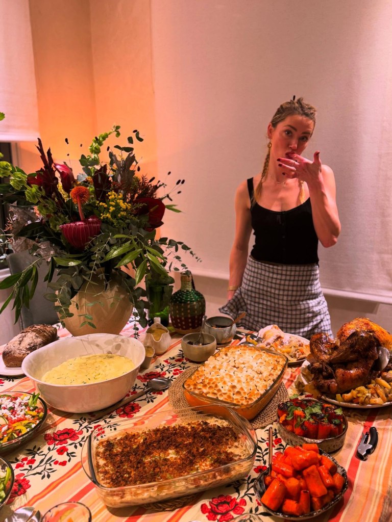 Amber Heard posing behind a Thanksgiving dinner table laden with food.