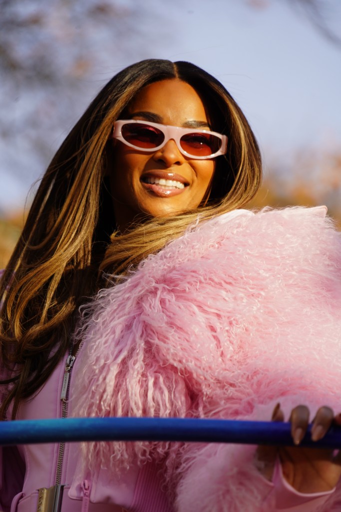 Ciara smiles, wearing pink sunglasses, a pink jacket, and a pink faux fur coat on a float during the Macy's Thanksgiving Day Parade.