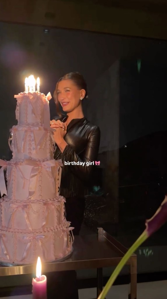 Hailey Bieber with a large pink birthday cake lit with candles.