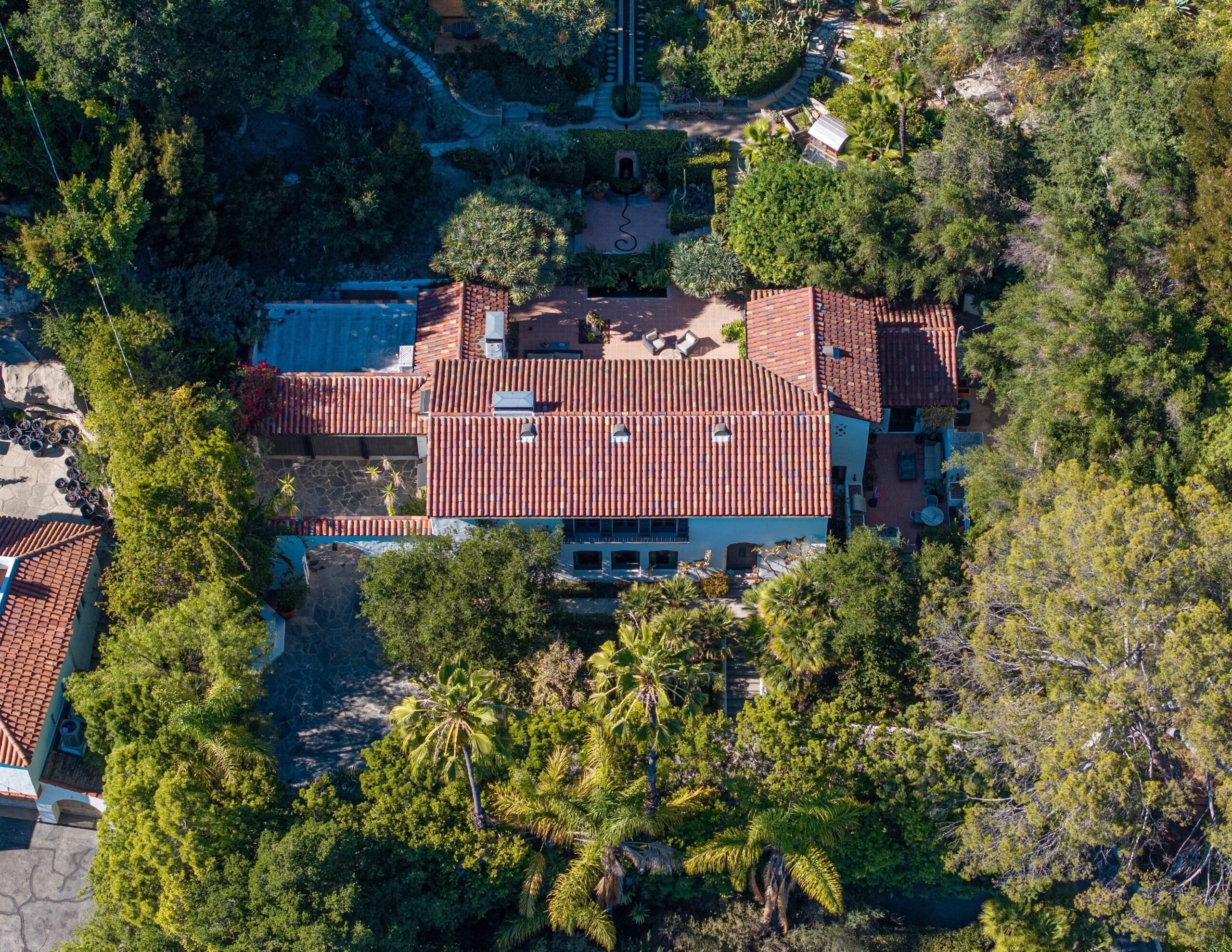 Aerial view of Aaron Paul's Los Feliz home with a red-tiled roof, surrounded by dense trees and green landscaping, and including patio areas.
