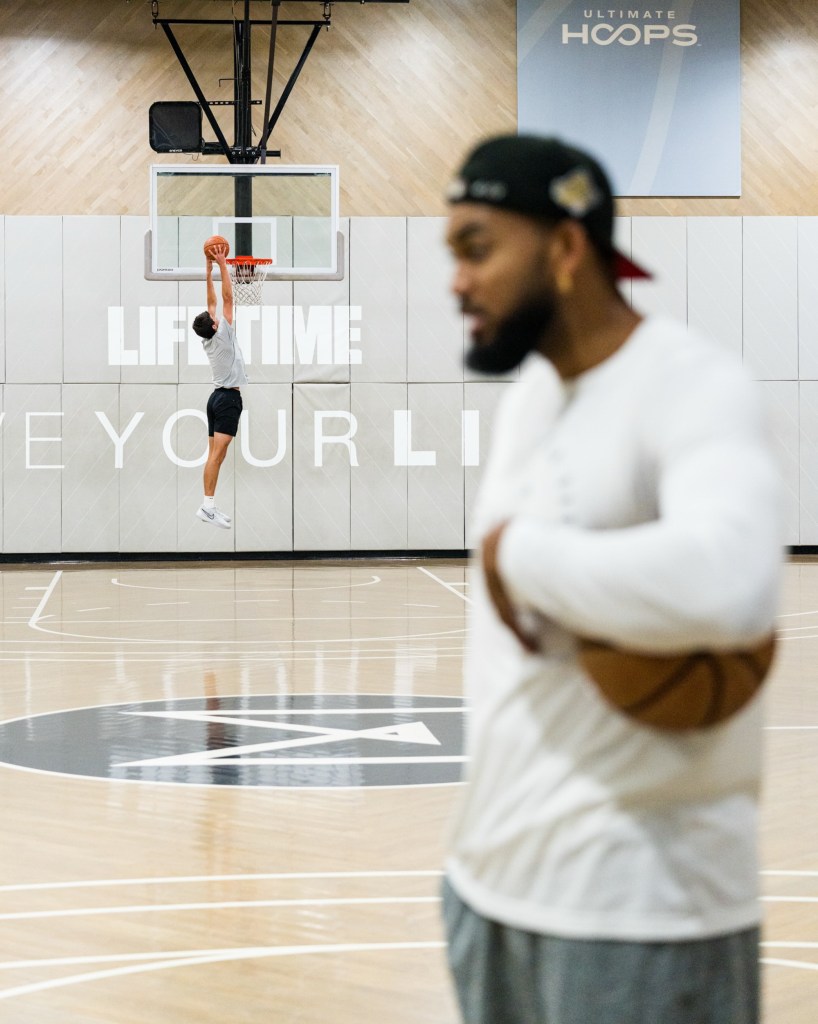 Jack Brady jumping to dunk a basketball as Karl-Anthony Towns (blurred) watches.