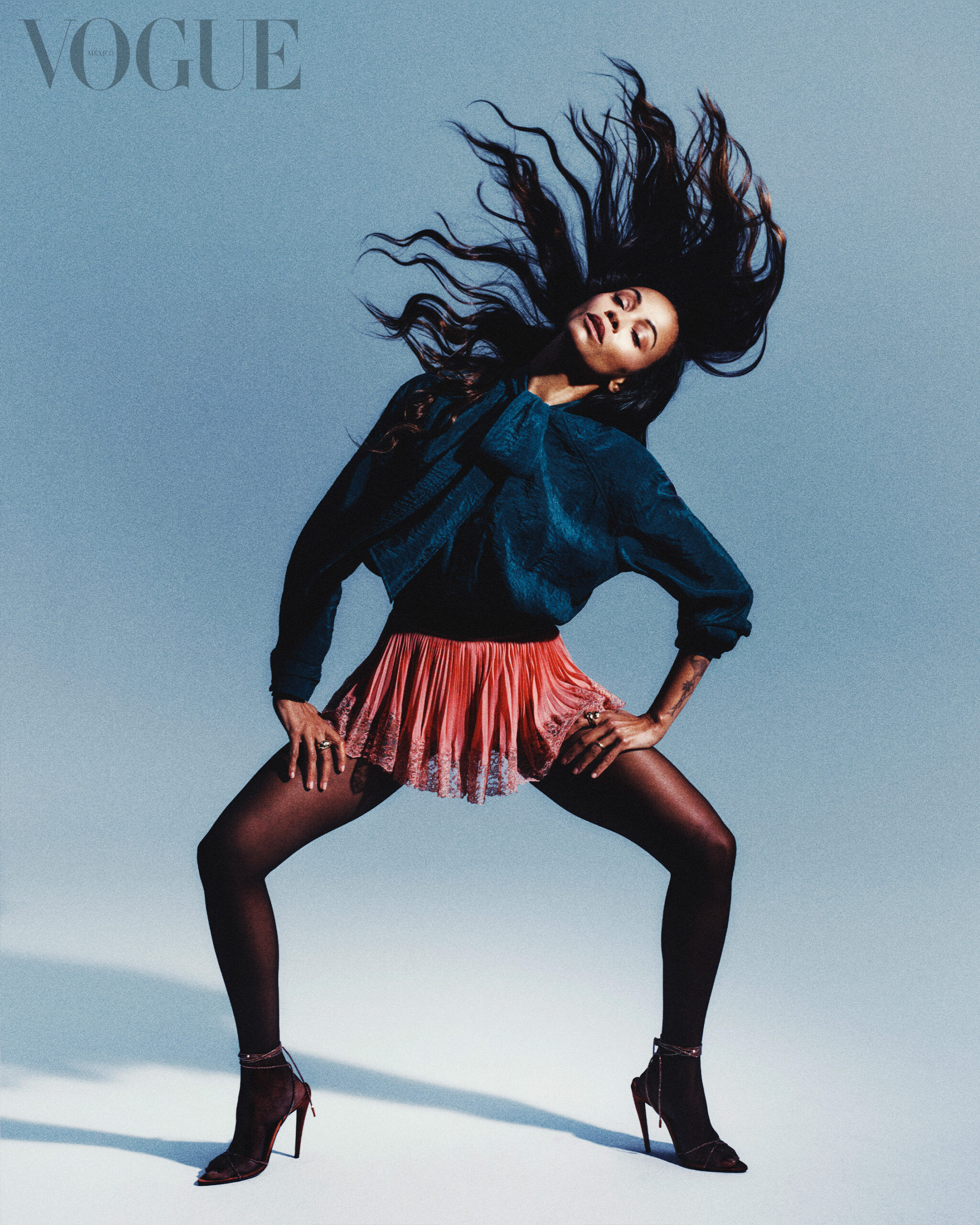 Zoe Saldana in a black tunic, red tulle miniskirt, and black tights against a blue background with "VOGUE Mexico" in the top left corner.