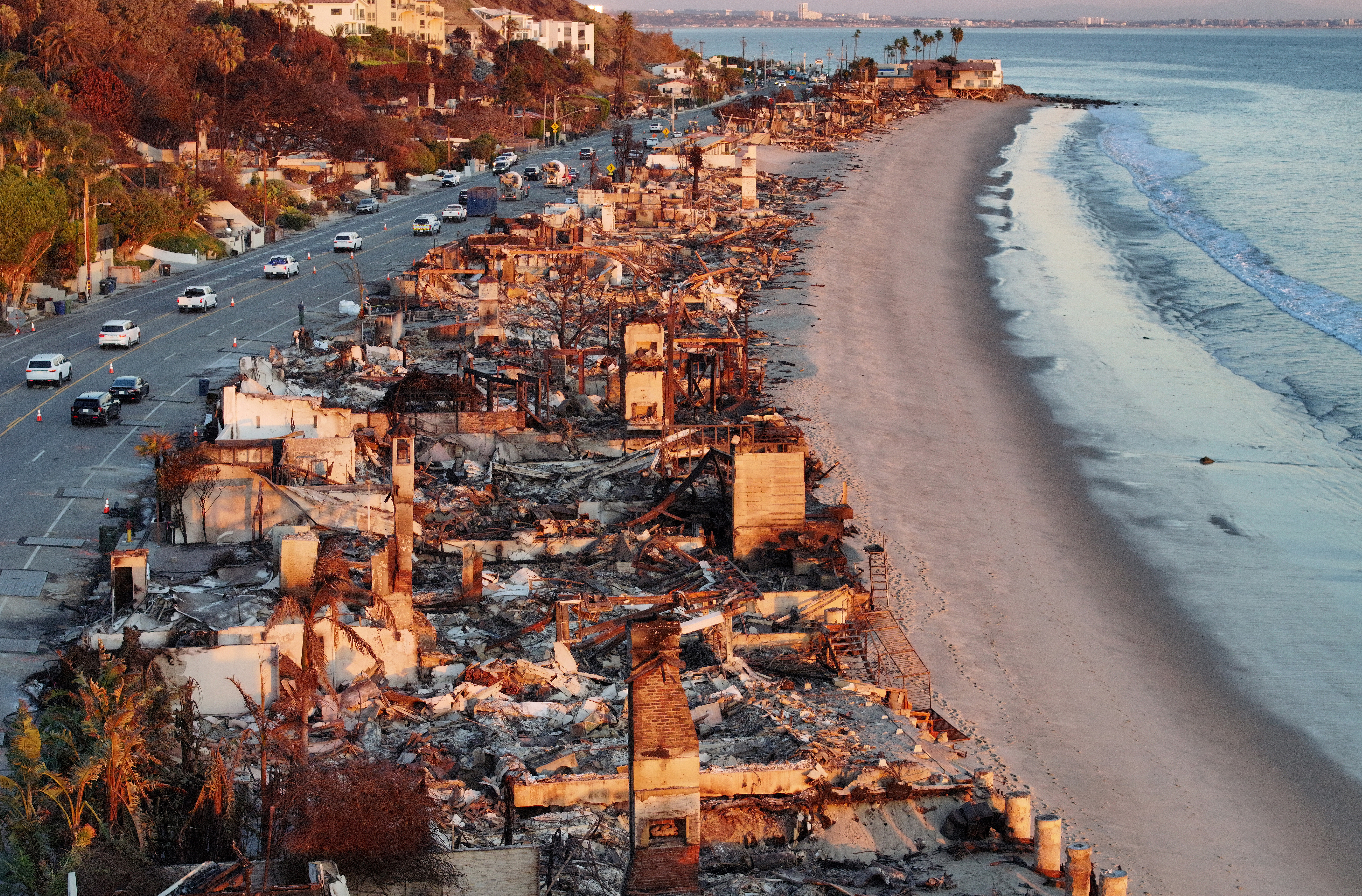 Aerial view of burnt beachfront homes and debris next to a highway in Malibu, California.
