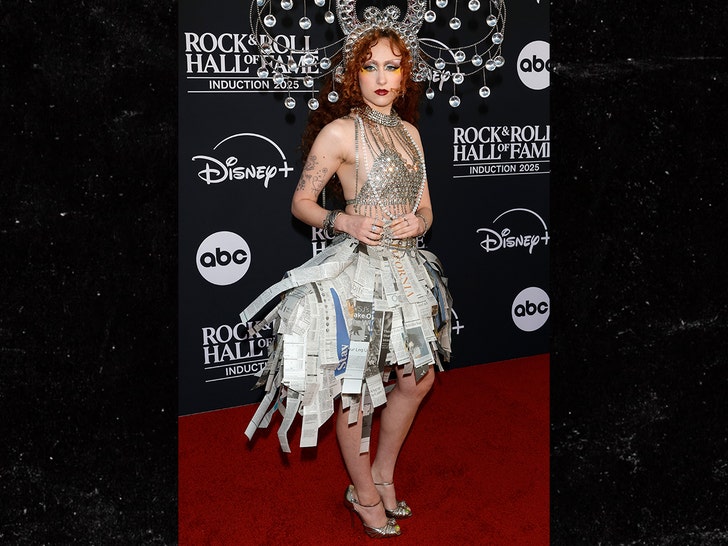 Chappell Roan on the red carpet in a silver dress with a newspaper-style skirt at the 2025 Rock & Roll Hall of Fame.