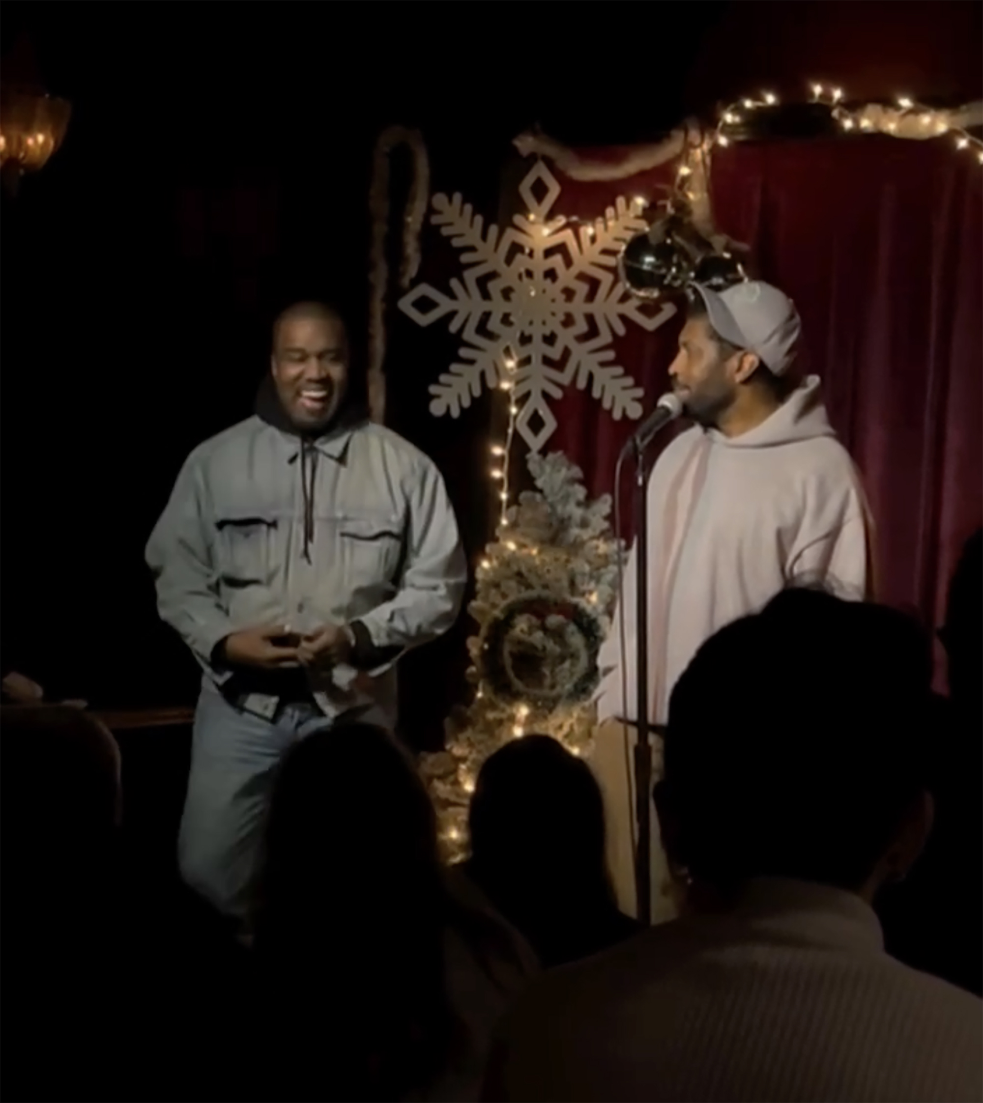 Deon Cole at a microphone with Kanye West laughing beside him.