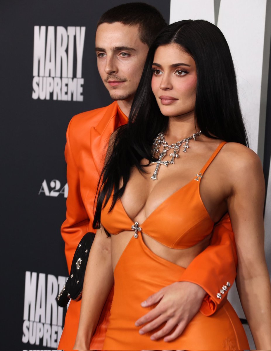 Full-length view of Jenner's neon orange gown and Chalamet's matching neon leather jacket and pants with orange boots at the Marty Supreme premiere red carpet.