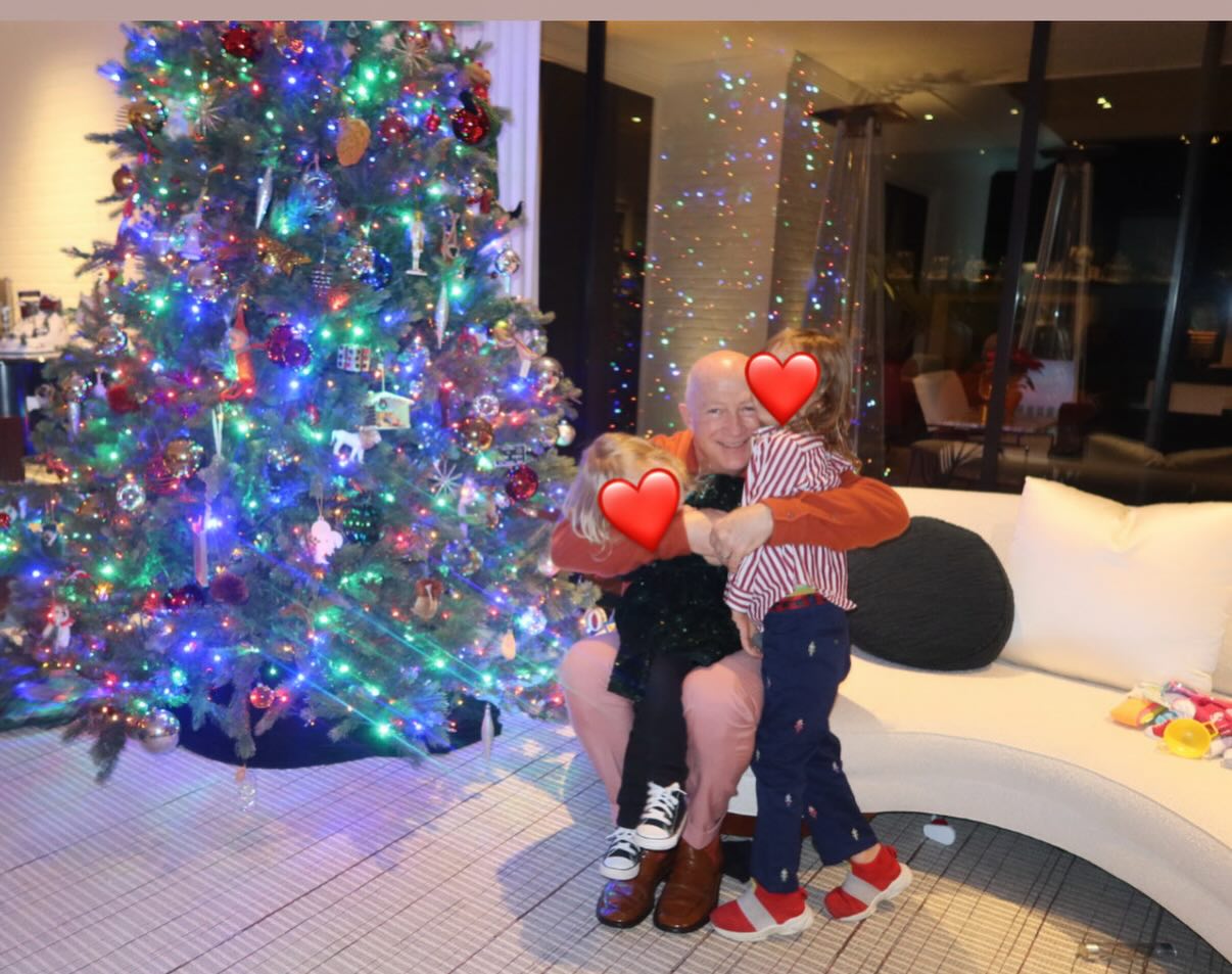 Bryan Lourd hugs grandchildren Kingston and Jackson in front of a Christmas tree, in the same room 25 years later.