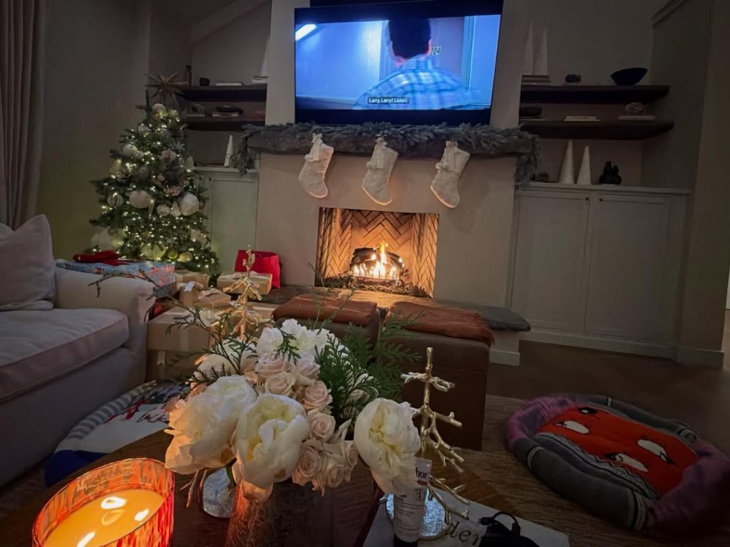 Cozy Christmas living room with three cream knit stockings over the fireplace and a lit tree.