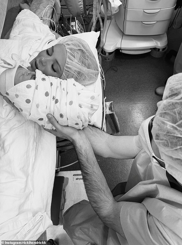 A medical professional holds Ricki Hendrick's swaddled newborn at her bedside
