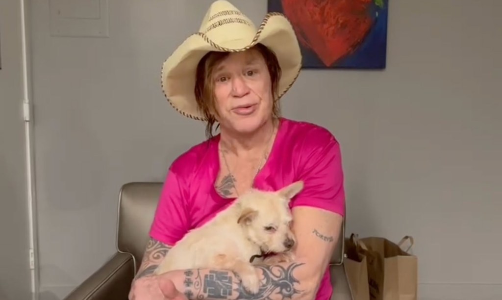 Mickey Rourke in a cowboy hat and pink shirt holding a dog during an Instagram video addressing the GoFundMe.