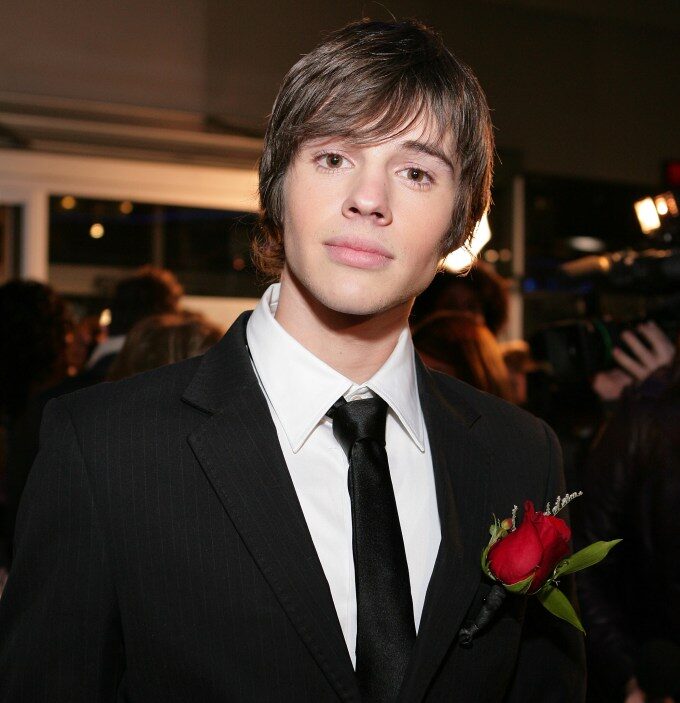 Actor Matt Prokop in a pinstripe suit with a red rose boutonniere at an event.