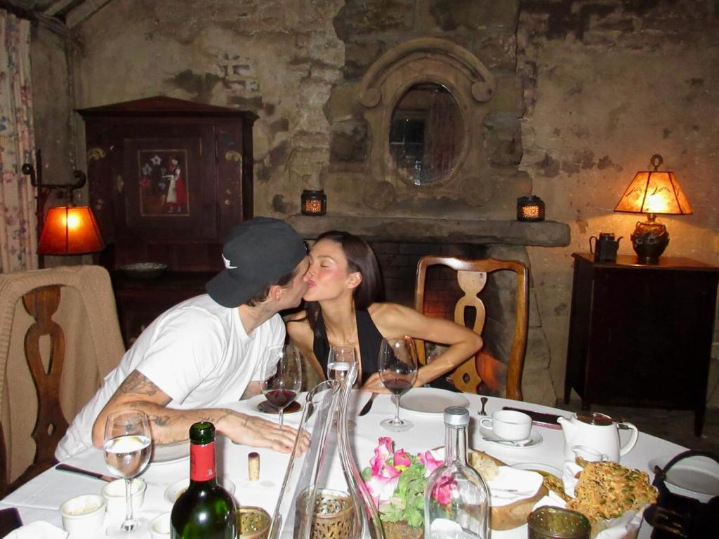 Brooklyn Beckham kissing Nicola Peltz at a dinner table during a romantic getaway.