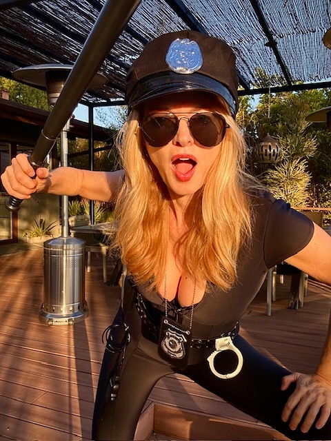 Heather Graham posing in a tight police costume and holding a baton.