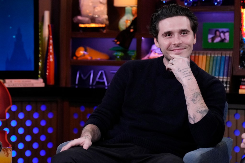 Brooklyn Peltz Beckham smiles, wearing a dark sweater with his tattooed arms visible, on "Watch What Happens Live with Andy Cohen."