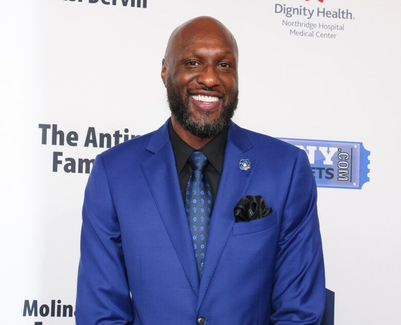 Lamar Odom smiling in a blue suit at an event.
