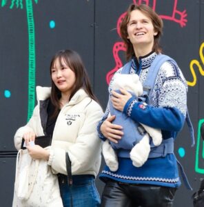 Ansel Elgort walks in New York City with a newborn in a chest carrier; both are bundled for winter.