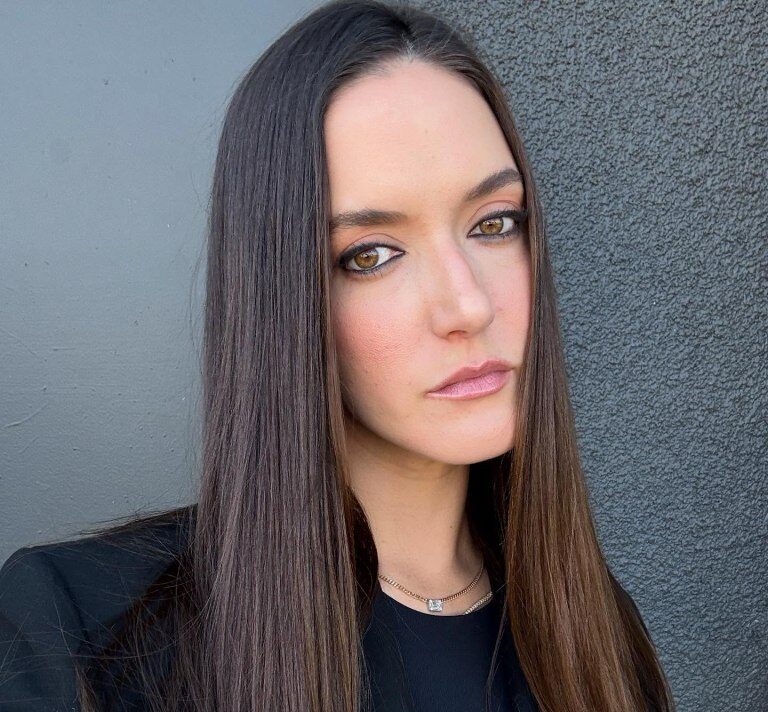 Alaia Baldwin with long brown hair, dark eyeliner, and a light pink lipstick.