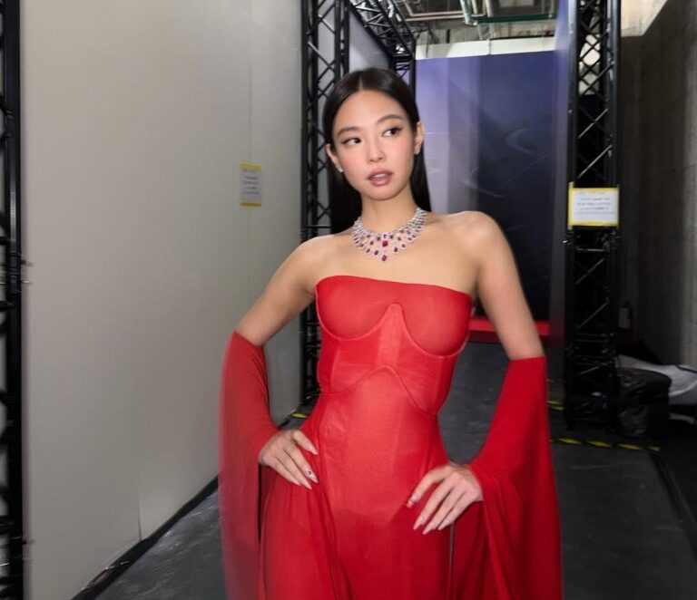 Jennie on the Taipei red carpet in a cherry-red Margiela gown, hood off, showcasing a ruby-and-diamond necklace.