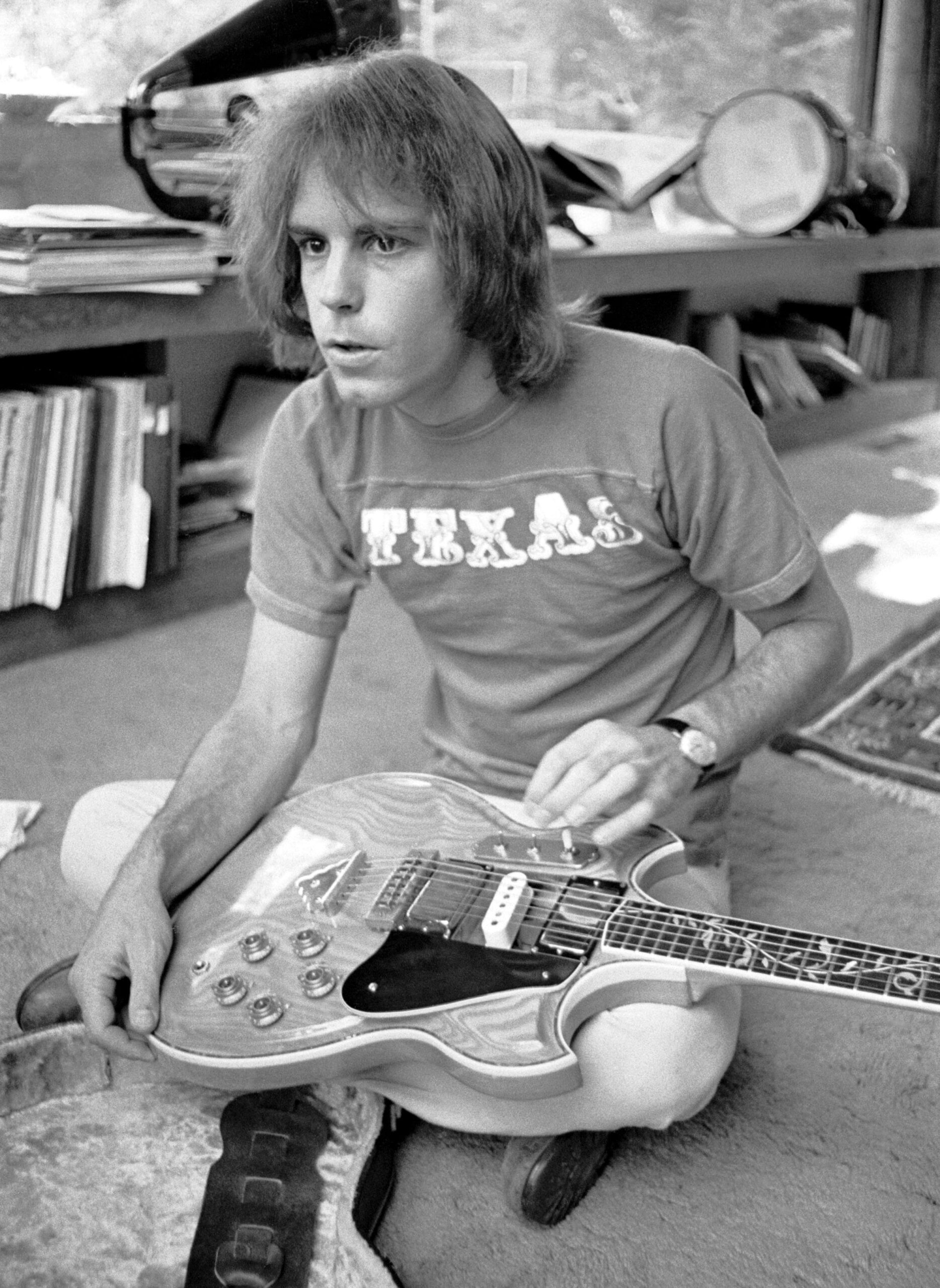 Bob Weir of Grateful Dead tuning his guitar while sitting on the floor.