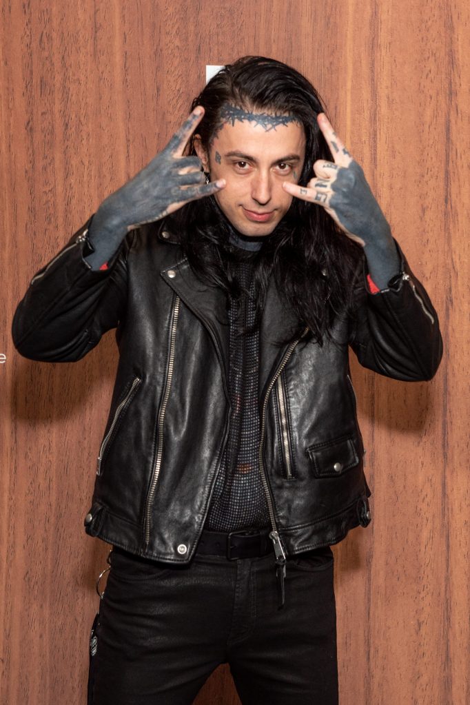 Ronnie Radke in a black leather jacket making rock hand signs.
