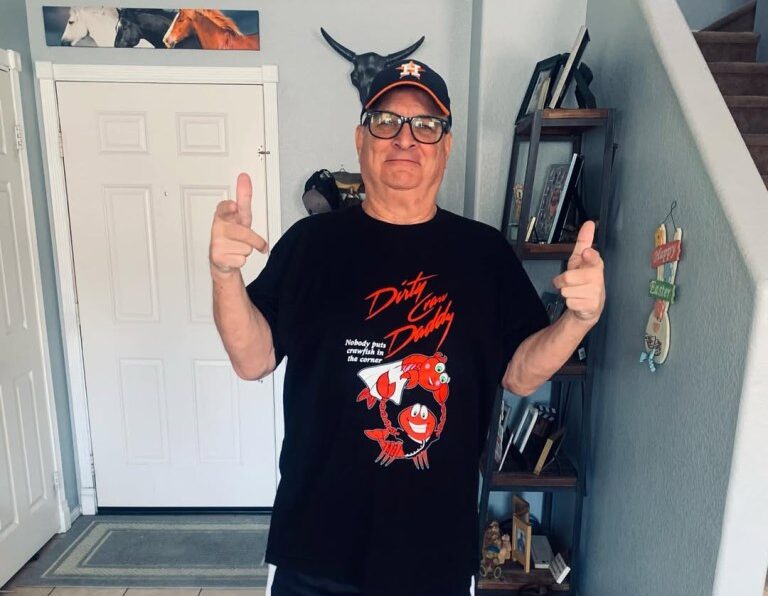 Sean Swayze wearing a "Dirty Craw Daddy" T-shirt and an Astros baseball cap, posing with finger guns.