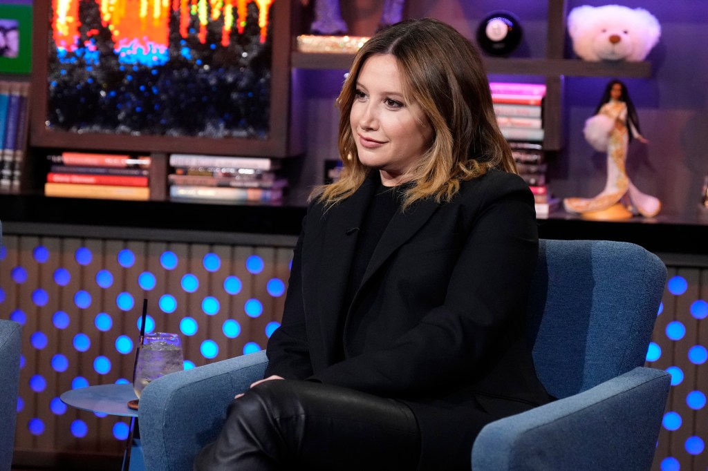 Ashley Tisdale sitting in a blue chair wearing a black blazer and leather pants.