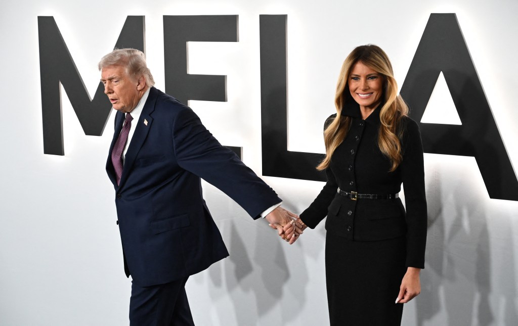 Donald Trump and Melania Trump hold hands in front of a large 'MELANIA' sign at the documentary premiere.