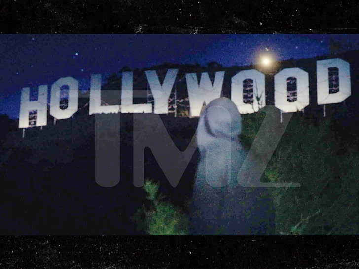 Sydney Sweeney climbs a Hollywood Sign letter at night while a film crew records, with bras visible along the structure. (TMZ)